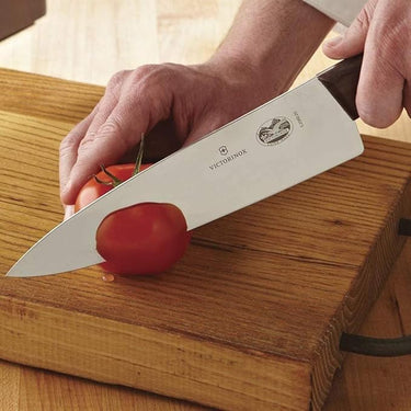 Person using a Victorinox carving knife to cut a tomato on a wooden cutting board.
